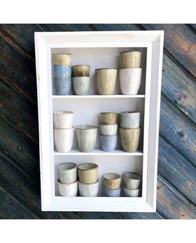 A white-framed shelf displays various boho coffee cups in shades of grey, beige, and white. A white-framed shelf displays various boho coffee cups in shades of grey, beige, and white.
