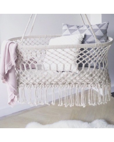 Een macramé hangwieg voor de baby, gevuld met een zachtroze deken en kussens met patroon.