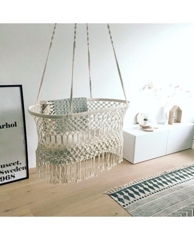 Een macramé hangwieg met franjes voor de baby, in een gezellige kamer met minimalistische inrichting.