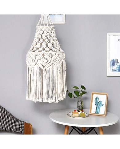 Een macramé vintage lampenkap met franjes hangt naast een tafeltje met een plant en decoratieve voorwerpen.