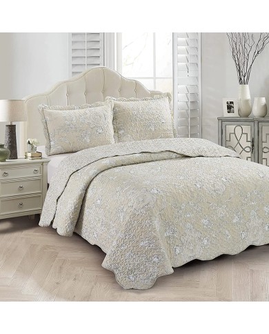 Elegante beige bedsprei met subtiele bloemenprint, geschulpte randen en bijpassende kussenslopen op een knus bed.