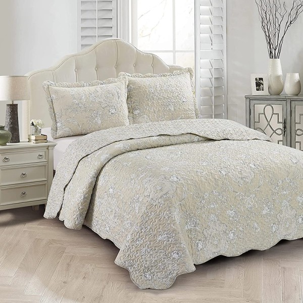 Elegante beige bedsprei met subtiele bloemenprint, geschulpte randen en bijpassende kussenslopen op een knus bed.