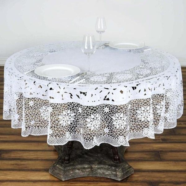 A round table adorned with a lace vinyl tablecloth, featuring two white plates and wine glasses.