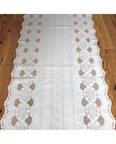 A white table runner made from vinyl featuring lace patterns and scalloped edges, on a wooden table.