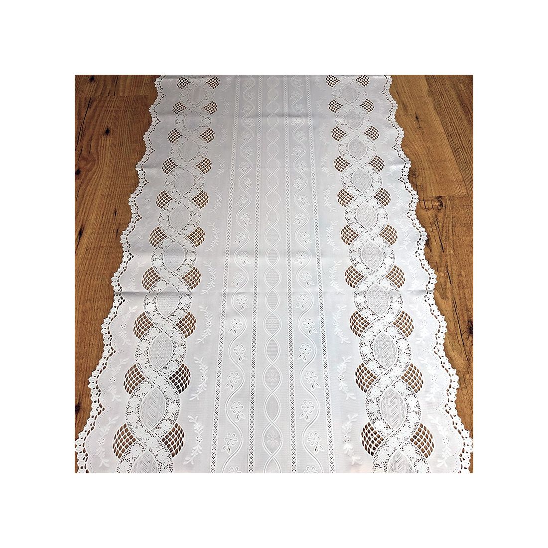 Een tafelloper wit gekleurd van vinyl met kantpatronen en schulpranden, op een houten tafel.