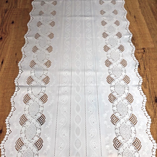 A white table runner made from vinyl featuring lace patterns and scalloped edges, on a wooden table.