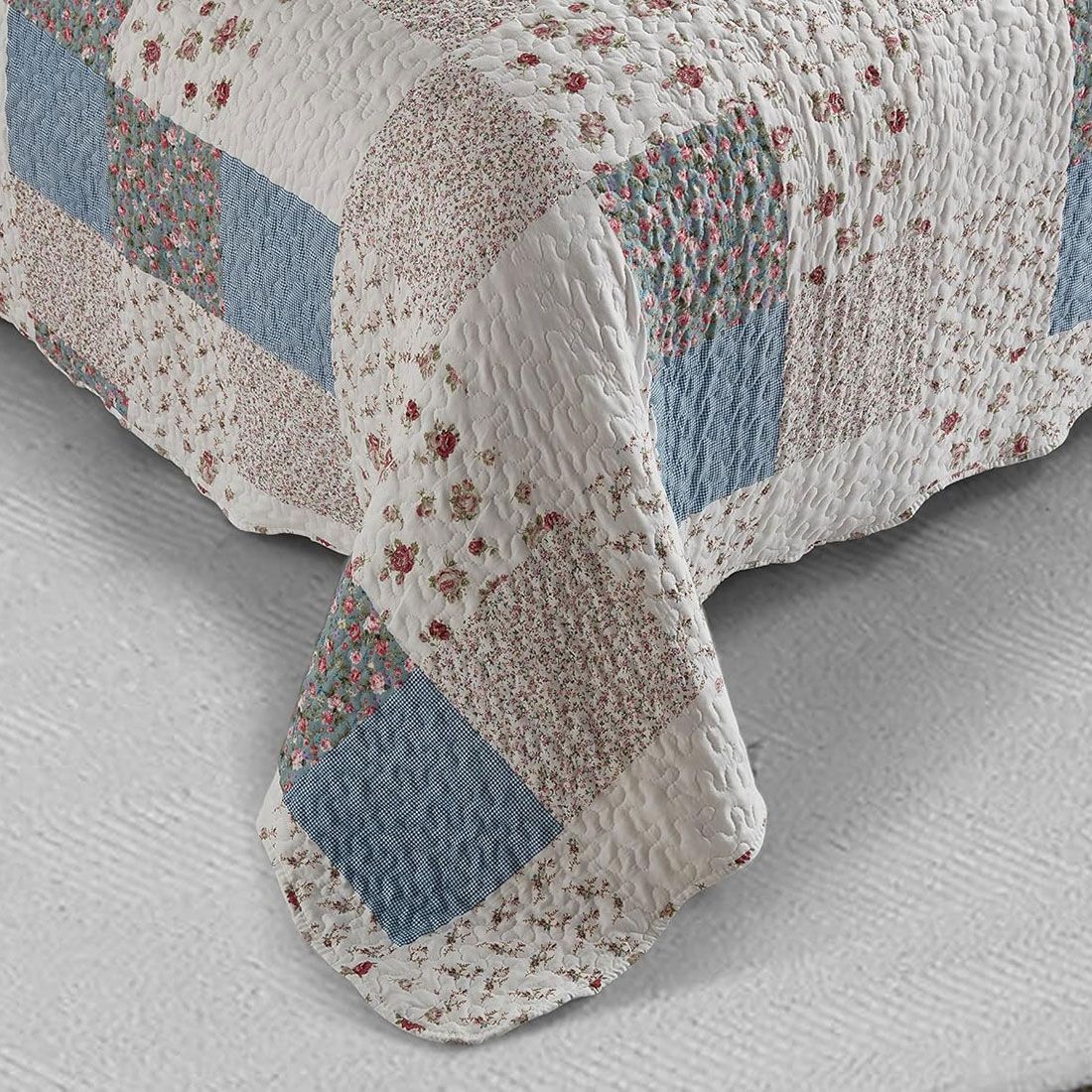 Detail of a floral bedspread showcasing blue and white patchwork, vermicelli stitching and scalloped edging.