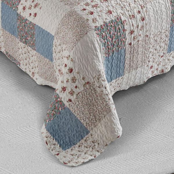 Detail van een bed sprei bloemen motief met blauw en wit patchwork, vermicellistiksels en geschulpte randen.