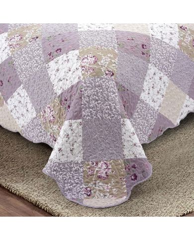 Detail van een bloemen sprei met een patchwork in lavendelprint, vermicellistiksels en geschulpte randen.