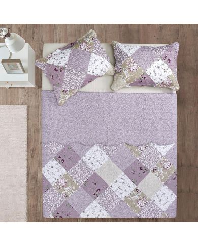 Bovenaanzicht van een bloemen sprei in patchwork ontwerp op een bed, aangevuld met bijpassende sierkussens.