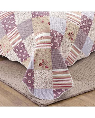 Detail van een bedsprei oud roze met bloemen, strepen en ruitjes, vermicellistiksels en geschulpte randen.