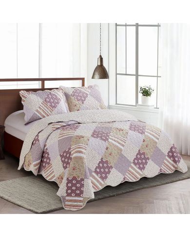 A cosy bed with a patchwork quilt in muted pinks and mauve tones, complemented by matching pillows, amidst a bright, airy room.