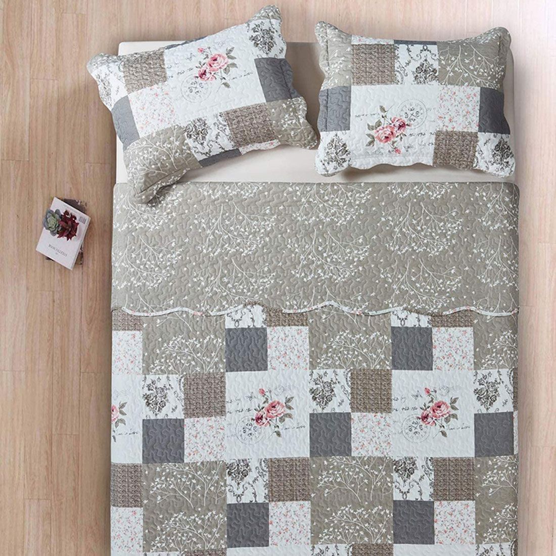 Quilted bedspread with a floral patchwork design in beige, complemented by matching decorative pillows. Quilted bedspread with a floral patchwork design in beige, complemented by matching decorative pillows.