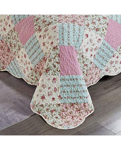 Detail van een bedsprei roze met gebloemde patchworkvlakken, vermicellistiksels en geschulpte randen.