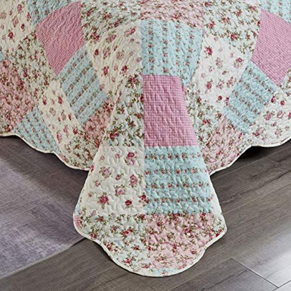 Detail van een bedsprei roze met gebloemde patchworkvlakken, vermicellistiksels en geschulpte randen.