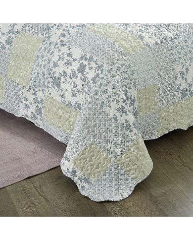 Detail of a blue bedspread showcasing floral patchwork squares, vermicelli stitching and scalloped edging. Detail of a blue bedspread showcasing floral patchwork squares, vermicelli stitching and scalloped edging.