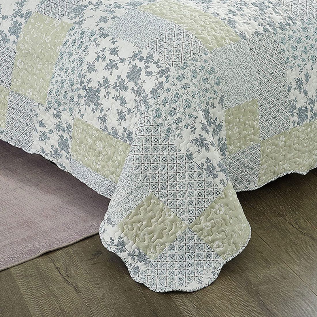 Detail of a blue bedspread showcasing floral patchwork squares, vermicelli stitching and scalloped edging. Detail of a blue bedspread showcasing floral patchwork squares, vermicelli stitching and scalloped edging.