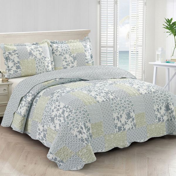 A quilt in blue and green tones on the bed in a well-lit bedroom with a sea view.