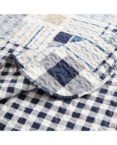 Close-up van een blauwe bedsprei, in blauw en wit patchwork met een verfijnde stikselstructuur. Close-up van een blauwe bedsprei, in blauw en wit patchwork met een verfijnde stikselstructuur.