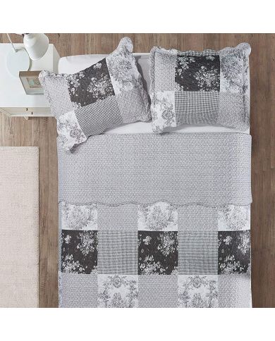 Bovenaanzicht van een patchwork grijze bedsprei op een bed, aangevuld met bijpassende sierkussens.