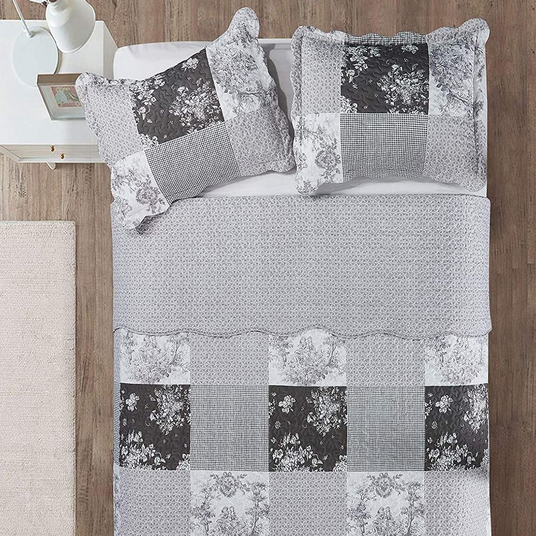 Top view of a patchwork grey quilt on a bed, complemented by matching decorative pillows. Top view of a patchwork grey quilt on a bed, complemented by matching decorative pillows.
