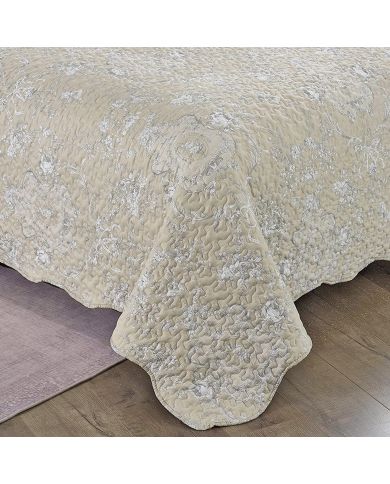 Detail of a beige quilt showcasing a subtle floral toile pattern, vermicelli stitching and scalloped edging. Detail of a beige quilt showcasing a subtle floral toile pattern, vermicelli stitching and scalloped edging.