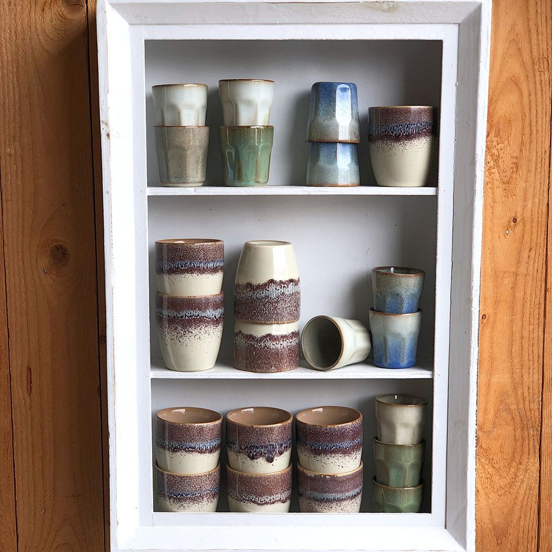 A display of artistically arranged handmade espresso cups in soft hues of blue and green.