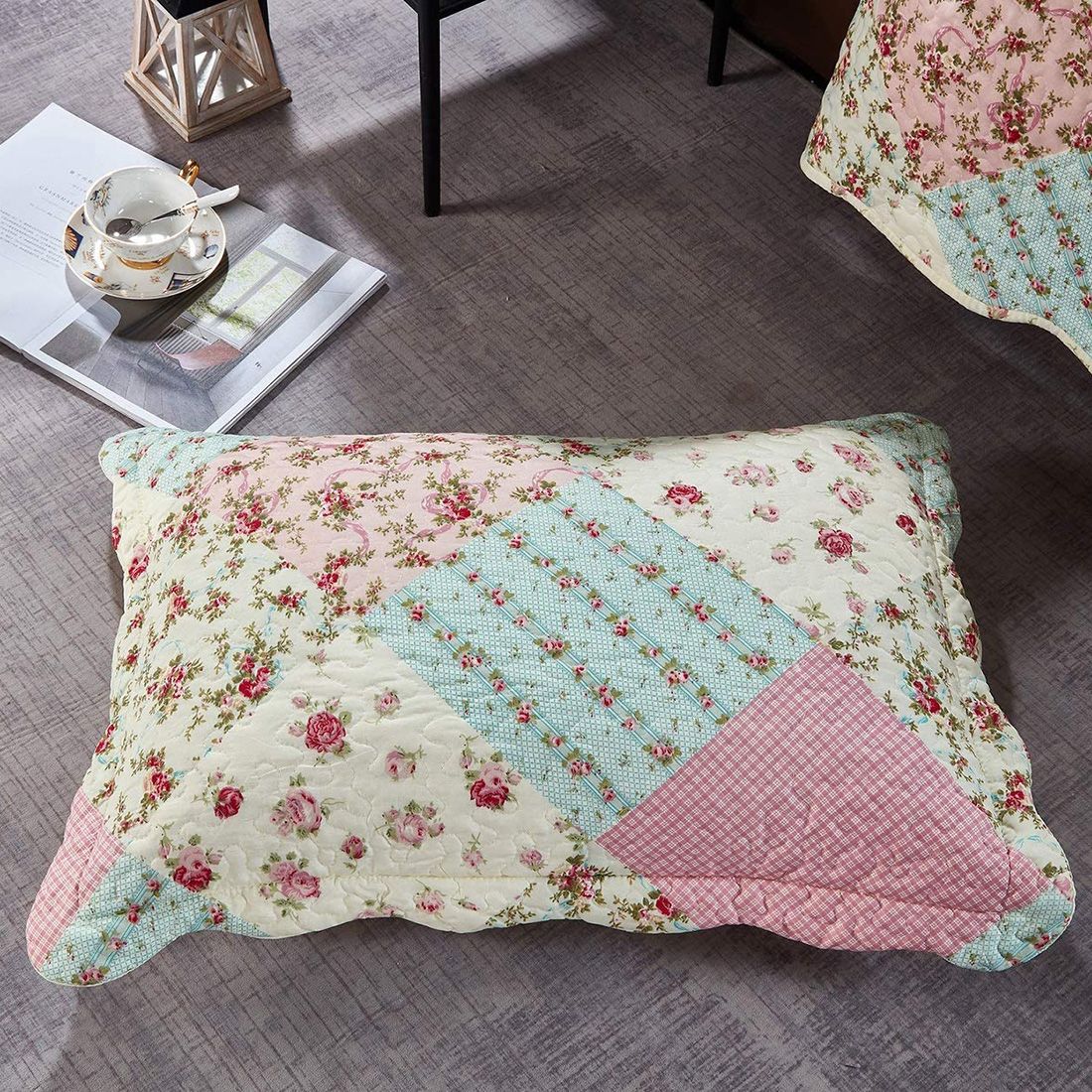A pink patchwork pillow in spring floral patterns rests on a textured grey floor.