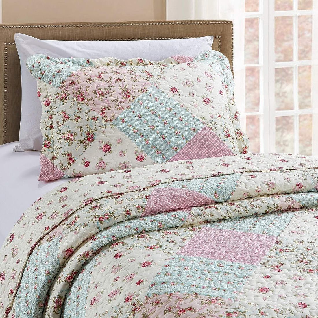 A pink and sage pillowcase with matching bedspread on a cosy bed by a window.