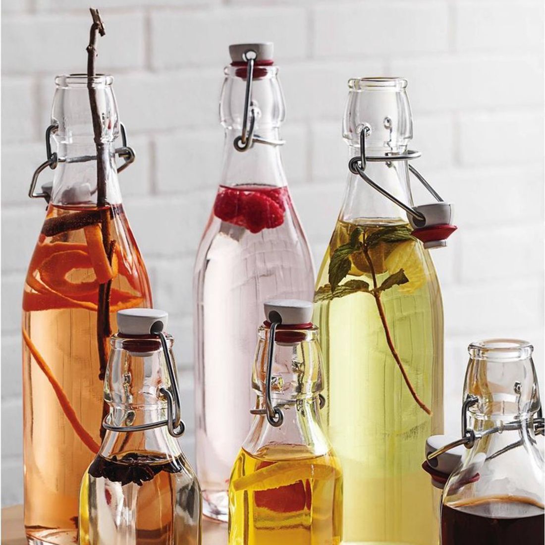 A variety of glass bottles filled with infused beverages, featuring fruits, herbs, and spices.