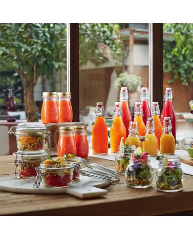 Colourful glass bottles of juice and jars of fresh salads are displayed on a wooden table.