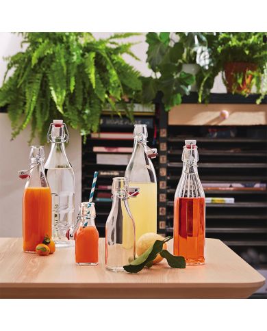 Op een houten tafel, omringd door groen, staan verschillende voorbeelden van de glazen beugelfles met kleurrijke drankjes.