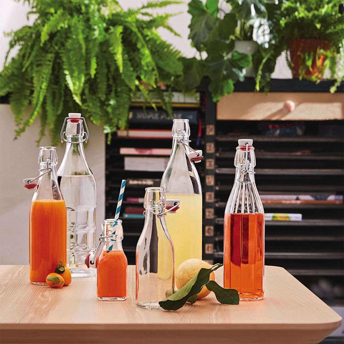 Op een houten tafel, omringd door groen, staan verschillende voorbeelden van de glazen beugelfles met kleurrijke drankjes.