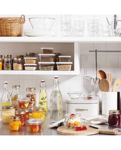 A tidy kitchen shelf displays jars of preserves, fresh ingredients, and kitchenware.