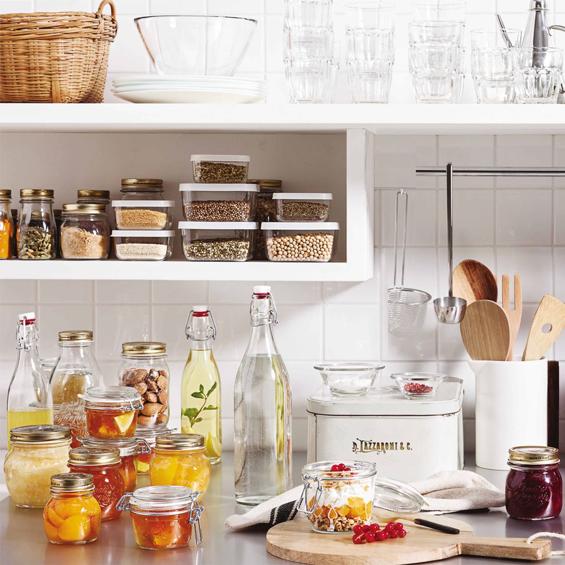 A tidy kitchen shelf displays jars of preserves, fresh ingredients, and kitchenware.