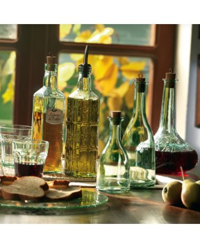 A cosy kitchen scene features green-tinted glass bottles of oil and vinegar, two glasses, bread slices, and pears.