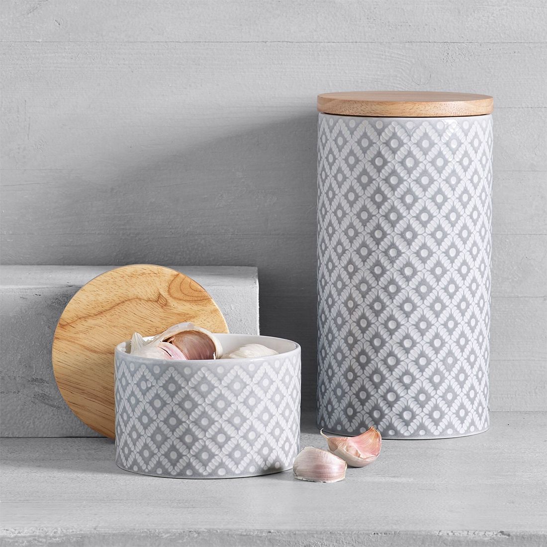 Two storage containers with a grey geometric pattern, one open with garlic cloves, the other with a wooden lid. Two storage containers with a grey geometric pattern, one open with garlic cloves, the other with a wooden lid.