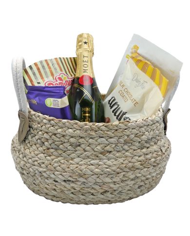 A seagrass gift basket holds a mini Moët champagne bottle, chocolates, and snacks. A seagrass gift basket holds a mini Moët champagne bottle, chocolates, and snacks.