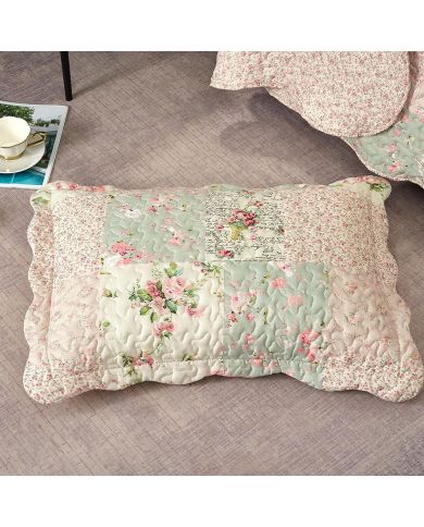 A pink patchwork pillow in delicate floral patterns rests on a textured floor.