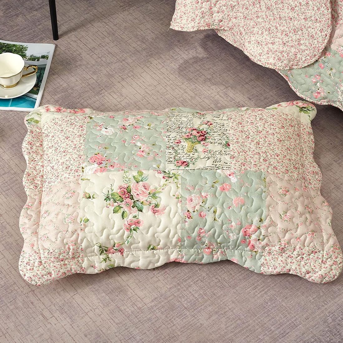 Een kussensloop groen en roze met patchwork en bloemmotieven rust op een vloer met structuur.