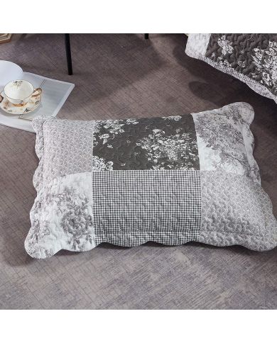 A patchwork pillow in Toile de Jouy patterns rests on a textured grey floor.