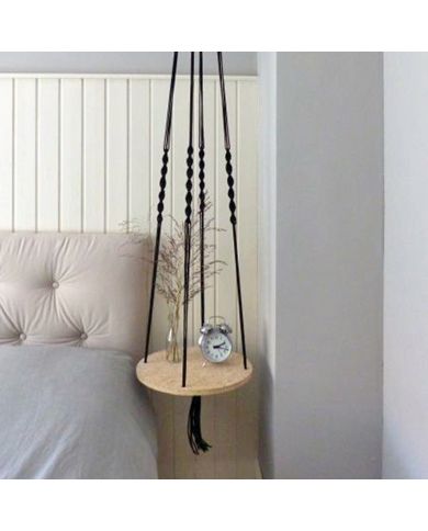 A macramé hanging bedside table made of wood, adorned with a small vase and an alarm clock.