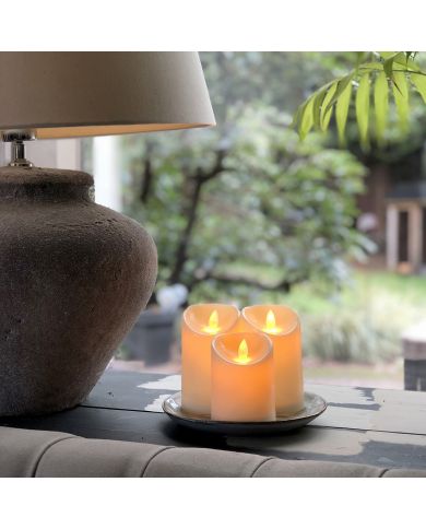 Een sereen tafereel met drie gloeiende LED stompkaars set op een bord, naast een stijlvolle lamp.