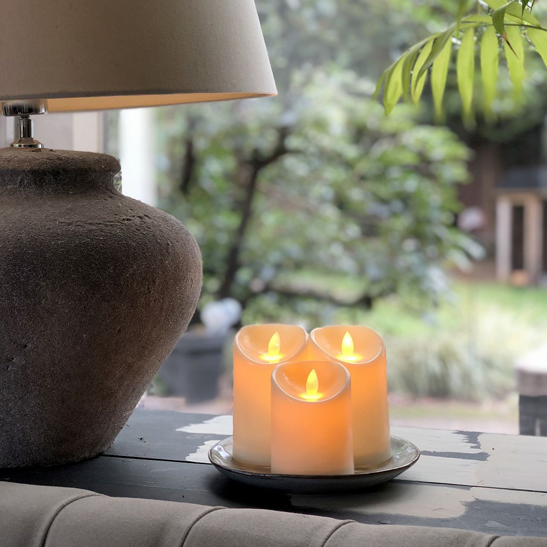 Een sereen tafereel met drie gloeiende LED stompkaars set op een bord, naast een stijlvolle lamp.