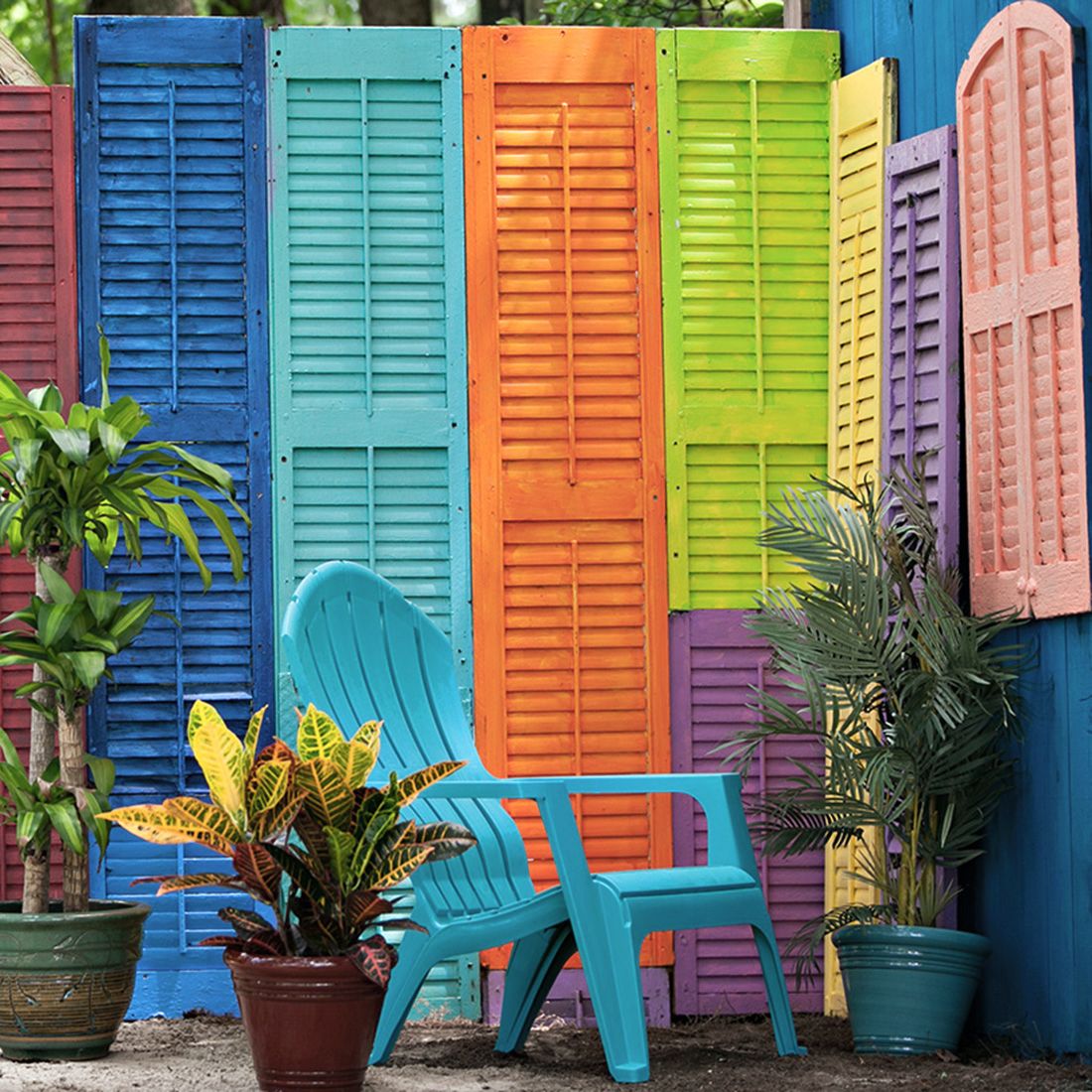 A vibrant outdoor scene featuring colourful wooden shutter panels and lush green plants in decorative pots.