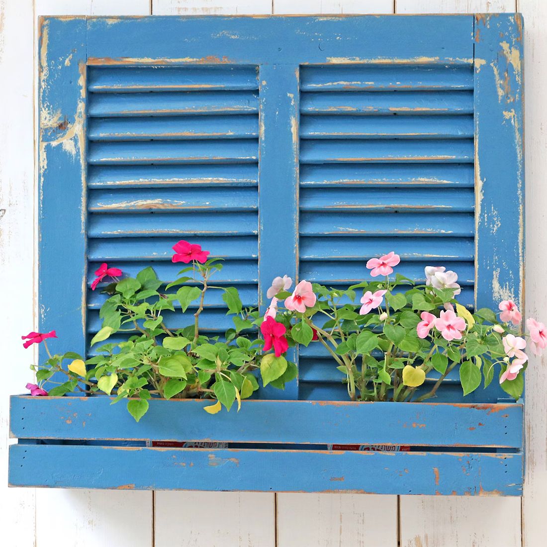 An upcycled planter made from bluewash shutters, adorned with vibrant pink and white flowers.