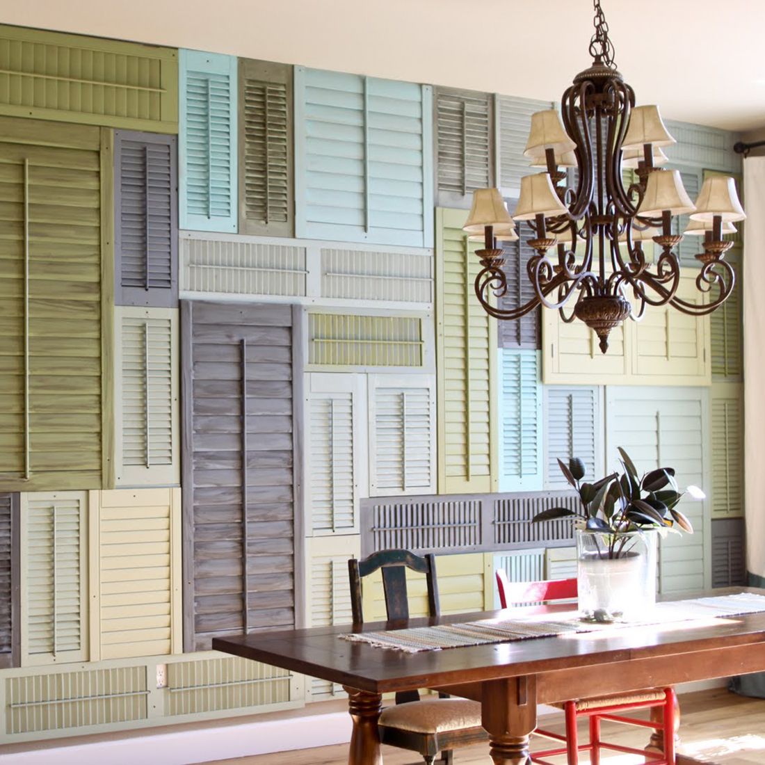 Een levendige muur van kleurrijke houten shutters en een elegante kroonluchter boven een houten tafel. Een levendige muur van kleurrijke houten shutters en een elegante kroonluchter boven een houten tafel.
