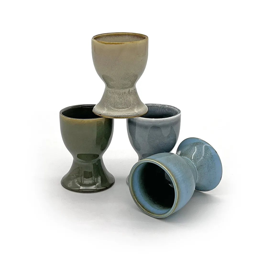 Four assorted ceramic egg cups with a reactive glaze finish, stacked creatively. Four assorted ceramic egg cups with a reactive glaze finish, stacked creatively.