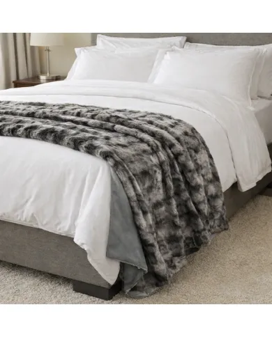 Cosy made bed with white sheets, pillows, and a silver grey faux fur throw blanket in a modern bedroom.