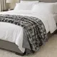 Een gezellig opgemaakt bed met witte lakens, kussens en een zilvergrijze plaid van imitatie bont in een moderne slaapkamer.